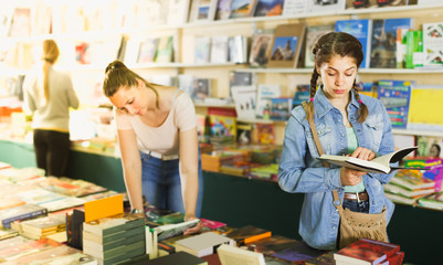 glad woman showing open book to smiling girl in book boutique