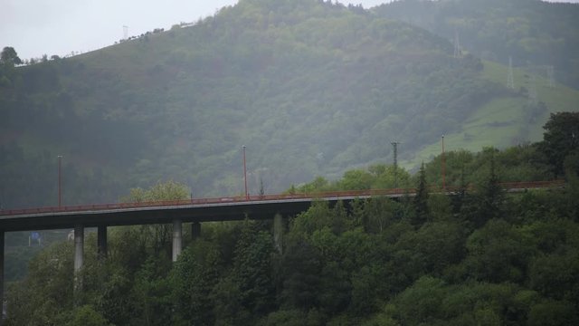 Panoramic shot of Bilbao with houses on top of forested hills. It s raining. Locked down real time medium shot