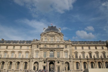 Inner courtyard and exterior of The Louvre Museum with walking tourists in a summer day