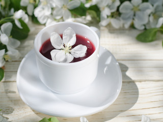 Fototapeta na wymiar White mug of tea on a wooden table, apple blossoms in the background. Sunny, side view