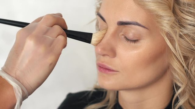 Make-up artist puts the foundation for makeup girl blonde, close up