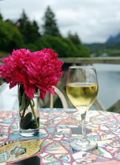 Glass of white wine on colorful table by vase of peonies