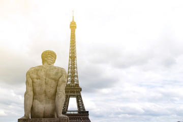 Paris France Eiffel Tower close-up with stone statue of seated man from the back looking at dusk sky