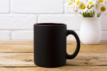 Black coffee mug mockup with chamomile bouquet in rustic vase