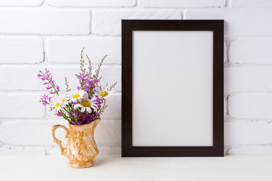 Black brown  frame mockup with chamomile and purple flowers in golden pitcher
