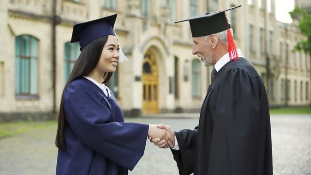 Presiding officer giving diploma to female student, shaking hand, convocation
