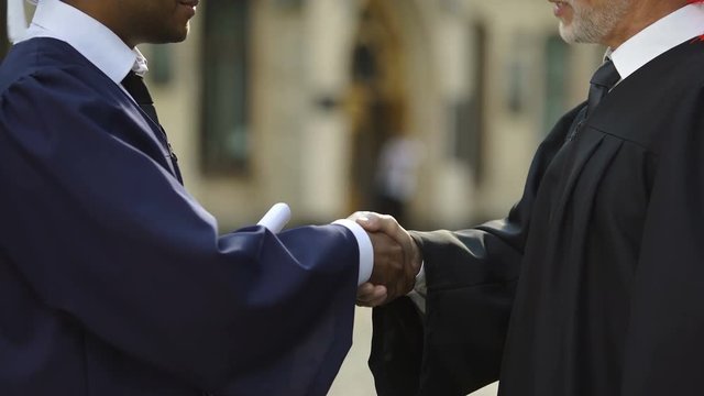 University Chancellor giving diploma to graduate student shaking hand, close up