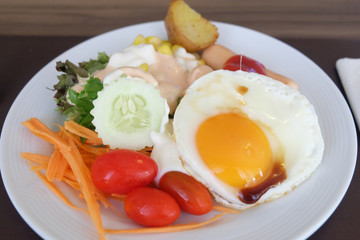 Salad vegetables, sausage, fried eggs in a white plate on the table