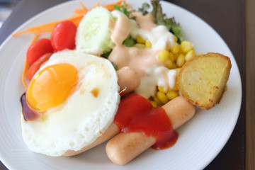 Salad vegetables, sausage, fried eggs in a white plate on the table