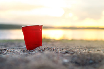 Red party cup in sand at sunset. Summer beach party concept with copy space.