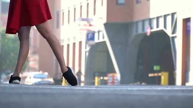 Slender female legs in sneakers standing on the square against the background of a shopping center