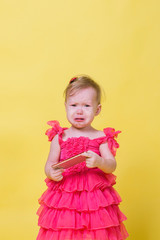 Girl toddler in a pink dress on a yellow background holding a smartphone and crying