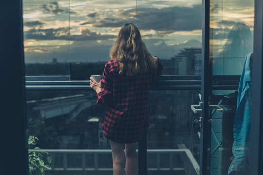 Woman drinking coffee on balcony at sunrise