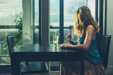 Fototapeta na wymiar Young woman having breakfast by the window in the city