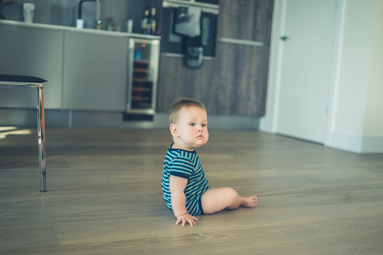 Little baby sitting on the floor in kitchen