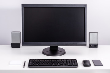 Black blank pc monitor stay on desk, around ordered space to work with keyboard, computer mouse, smartphone, speakers, pen and sticky notes.