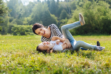 Cheerful mother and daughter goofing around on grass in park