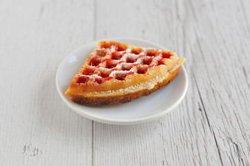 Waffle with raspberry filling on a white plate on a wooden background