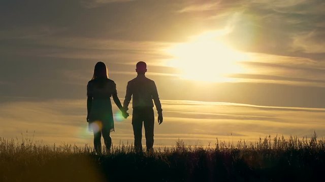 Silhouette of a young couple walking toward the sunset. The concept of love.