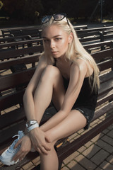 Fototapeta na wymiar Fashionable blonde model in stylish clothes posing on a bench in the park