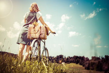 Woman walking with retro bicycle and basket on flower meadow