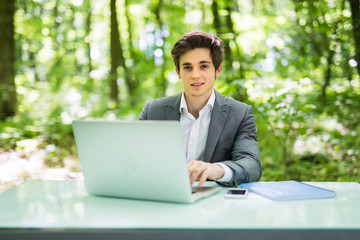 Businessman working on laptop computer in the forest at office table and smile at camera. Business concept.