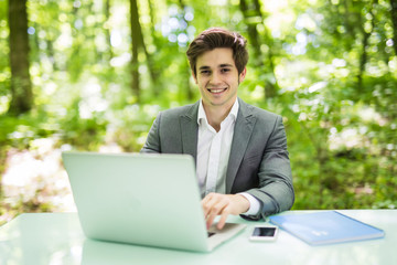 Businessman working on laptop computer in the forest at office table and smile at camera. Business concept.