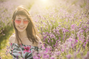 Lavender field. Smiling woman sitting through blooming flowers. Pink heart shaped sunglasses. Summer sunset soft light