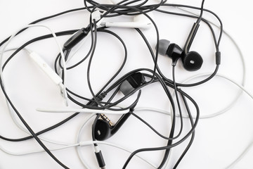 Fototapeta na wymiar Black and white tangled little headphones lie on a white isolated background. Horizontal frame