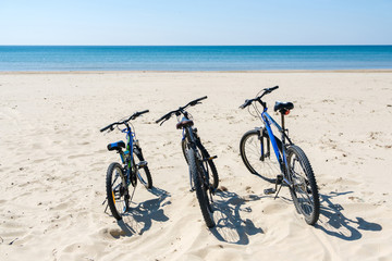 Obraz premium Three bicycles are on the beach on sea background