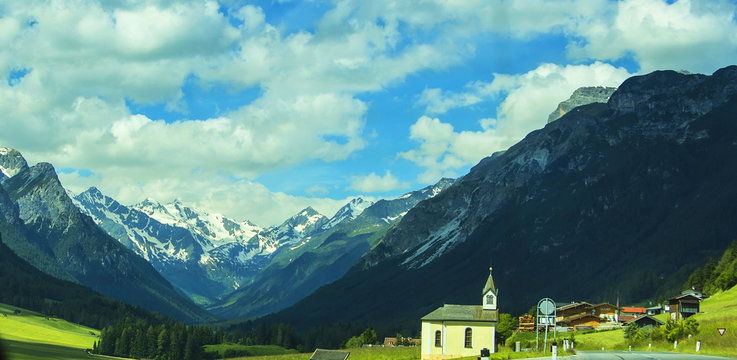 Background view of the panorama of the Alpine peaks, the sky and a beautiful Christian church in an alpine village in Tyrol