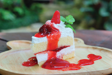 Piece of fresh strawberry cheesecake with strawberry sauce served on wooden plate.