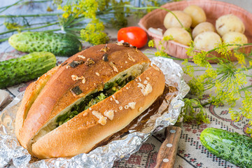  Bread for a picnic. Homemade bread with cheese, garlic, green onion and herbs in foil on a linen tablecloth. Next to the fresh vegetables and boiled potatoes.