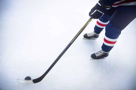 the legs of a hockey player skating on ice with stick and puck close up