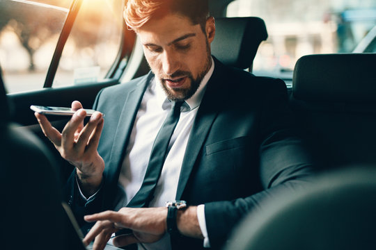 Businessman travelling by car using smart phone and checking tim