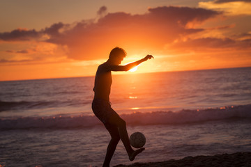 Fototapeta na wymiar Young male playing football on the beach at sunset