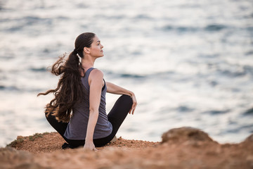 Fototapeta na wymiar Yogi girl does twisting on a cliff by the sea