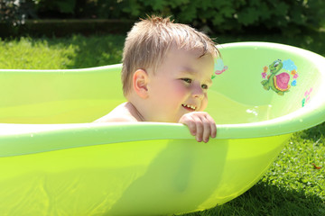 Child playing with water in little plastic bath outdoors in the garden.