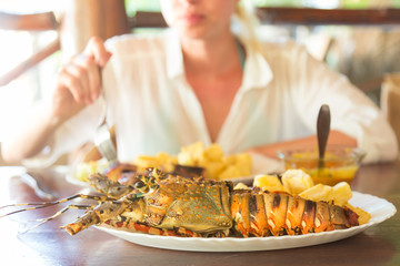 Lady on tropical vacations eating grilled lobster served with potatoes and coconut sauce.