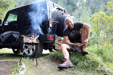 Mann grillt am Camping Platz vor SUV