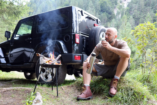 Mann grillt am Camping Platz vor SUVMann grillt am Camping Platz vor SUV
