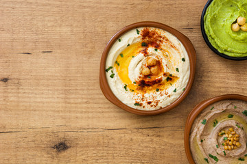 Different hummus bowls. Chickpea hummus, avocado hummus and lentils hummus on wooden table

