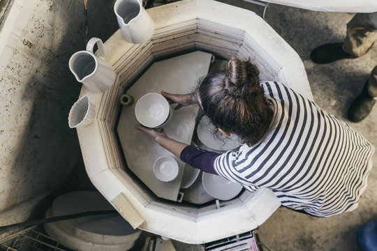 Woman taking ceramic bowls out of kiln