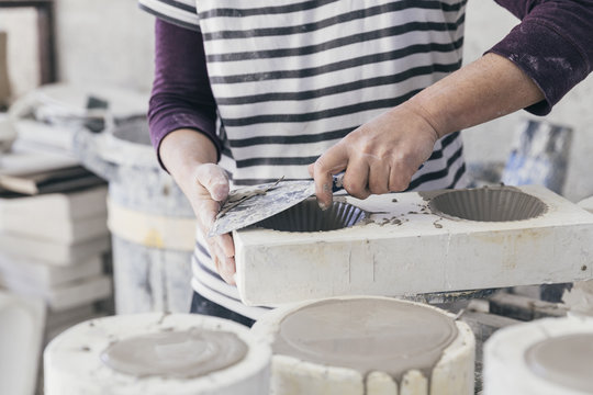 Hands of a ceramic artist removing excess material from mould