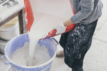 Person mixing white glazing paint in a bucket