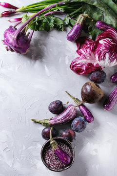 Assortment raw organic of purple vegetables mini eggplants, spring onion, beetroot, radicchio salad, plums, kohlrabi, flower salt over gray concrete background. Top view with space. Food frame