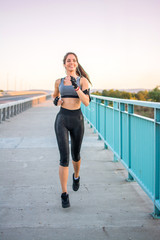 Beautiful athlete woman running over bridge during sunset.