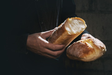 Loaf of fresh baked wheat bread in man's hands in sunshine. Rustic day light in dark room. Toned...