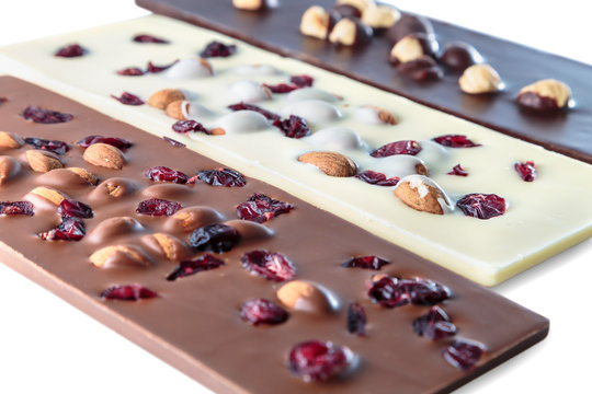 chocolate bars with nuts, dried cherries and almonds lying on a white surface