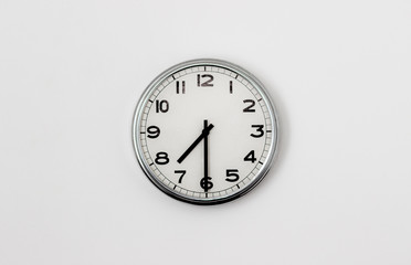 White Clock hanging on a white wall showing time 7:30